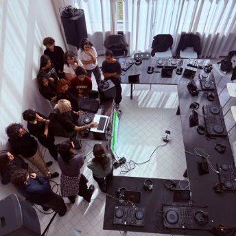 Overhead view of attendees seated around a horseshoe of DJ decks