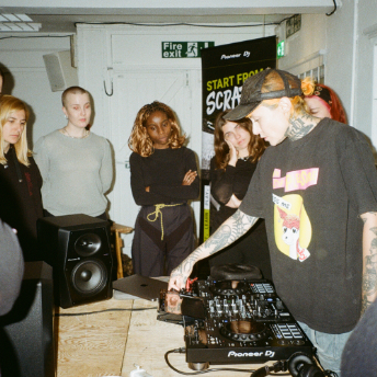 Tutor playing on CDJs as attendees watch beside the Start From Scratch banner