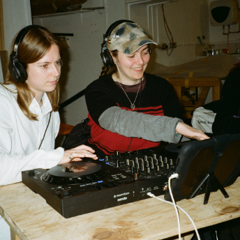 Two attendees in headphones sharing a DJ controller at the ICA