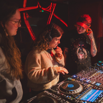 Attendee in headphones cueing a track on the CDJs while others look on